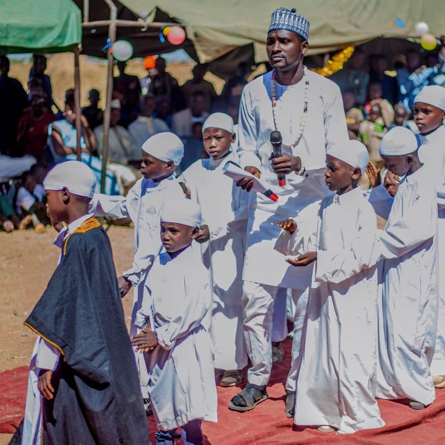 Pupils in white robes performing a Cultural Day procession on a red mat