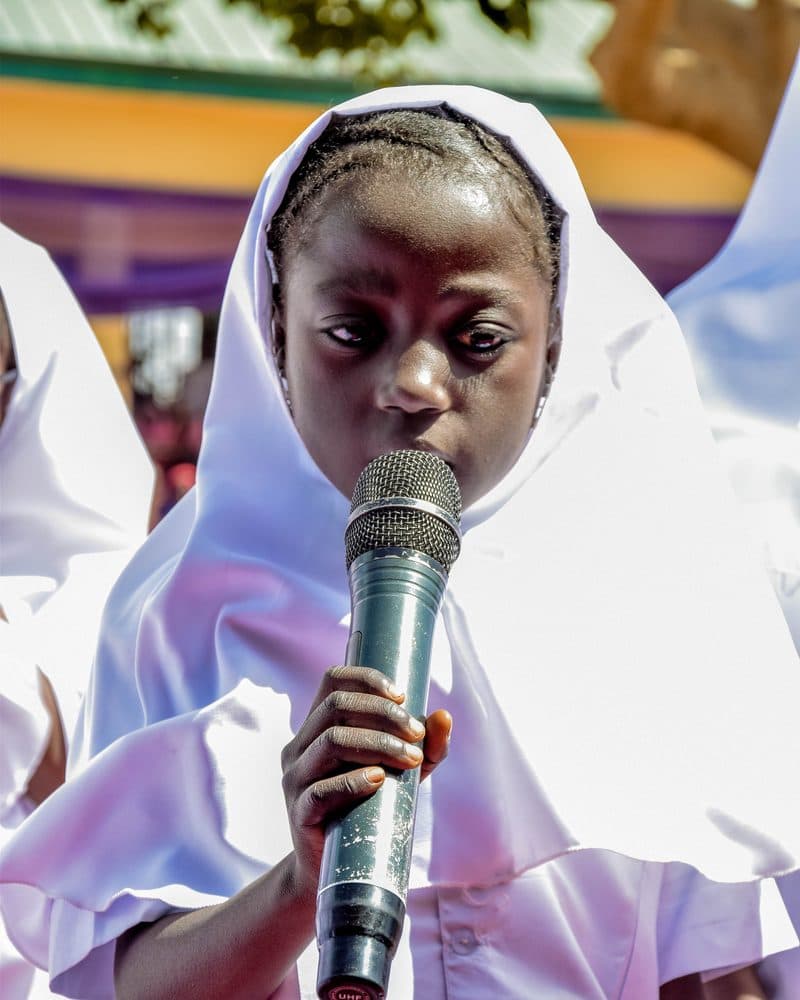 A pupil in a white nurse's uniform speaking into a microphone